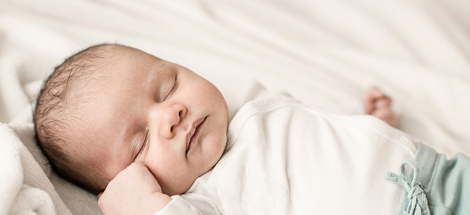 A newborn baby sleeping peacefully on a white blanket, wearing a white outfit